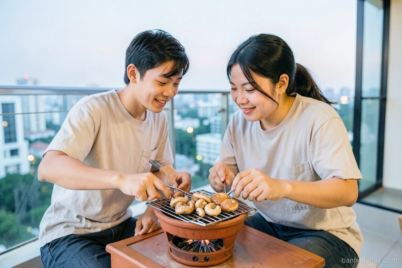 Two young Vietnamese friends grilling king oyster mushrooms on a small clay charcoal stove on an open apartment balcony at dusk, banh mi on the grill, side angle