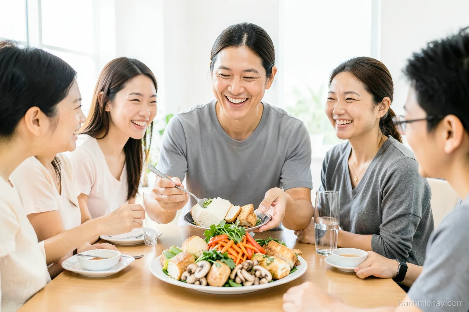 Vietnamese host explaining a platter of banh mi fillings, tofu, mushrooms, pickled carrot and herbs, to smiling foreign guests at a home dining table, bright daylight, wide shot